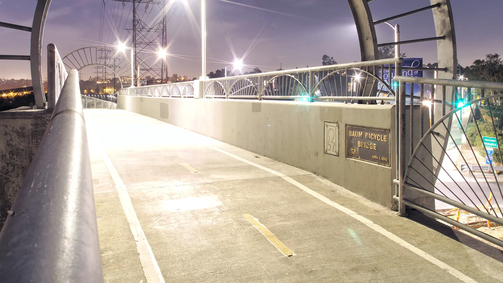 Passerelle cyclable éclairée la nuit, avec rambardes courbes et lampadaires