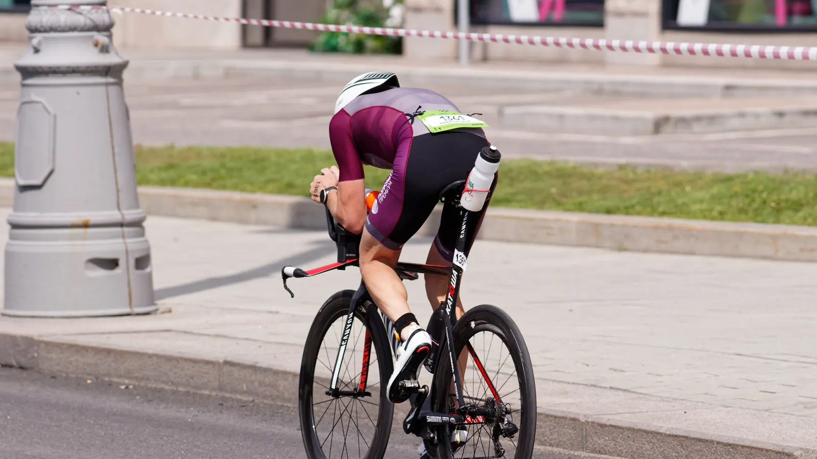 Coureur en position aérodynamique sur un vélo de contre-la-montre, vu de dos, sur une rue pavée