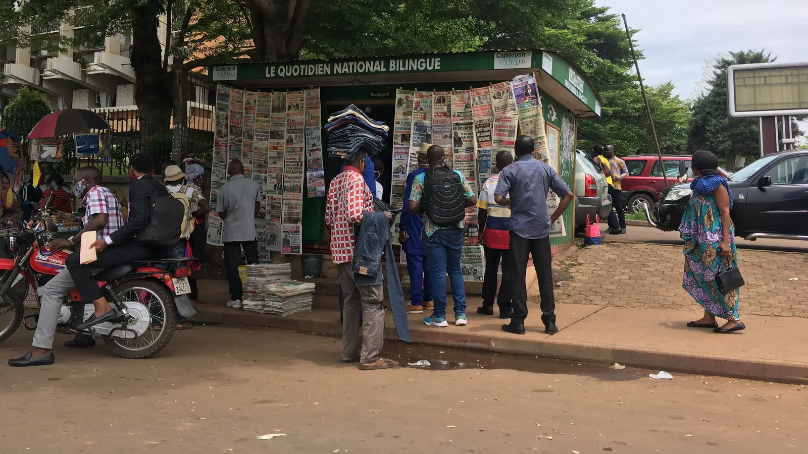 Kiosque à journaux dans une rue de Yaoundé, avec des lecteurs devant les unes affichées